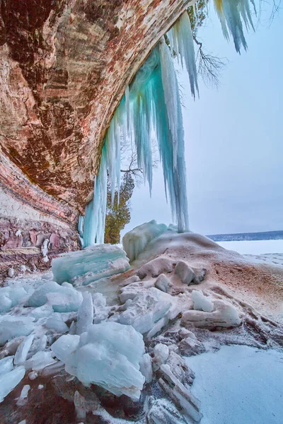 Eishöhlenöffnung auf Felsen und See mit blauen Eiszapfen — Stockfoto