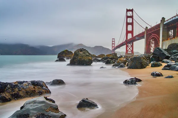 Bulanık su dalgalarının görüntüsü Golden Gate Köprüsü 'nün güneybatısındaki kumlu ve kayalık sahile vuruyor.