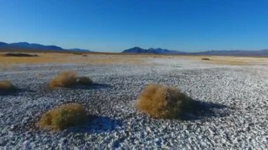 Küçük çalılar ve geniş dağlarla beyaz kum çölünü geçerken çekilmiş bir video.