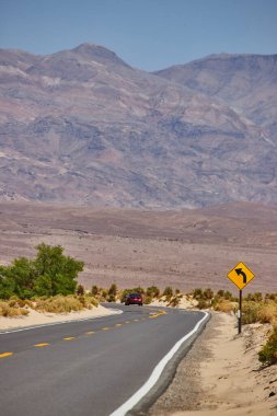Kumlu çöl ve dağlarla çevrili asfalt yolda keskin bir dönüş yapan kırmızı araba görüntüsü