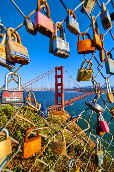 Image of Locks covering chain linked fence with opening to sunset view of Golden Gate Bridge in San Francisco