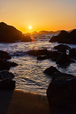Kum Sahili 'nin canlı günbatımının yanındaki kayaların üzerinde dalgalar.