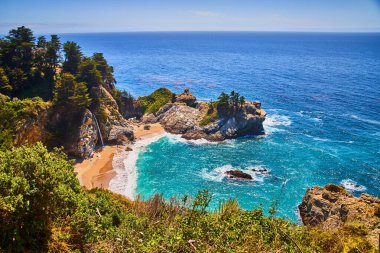 McWay şelalesinin, kumlu sahilleri ve renkli okyanus suyuyla kıyı koyunda gizlenmiş görüntüsü.