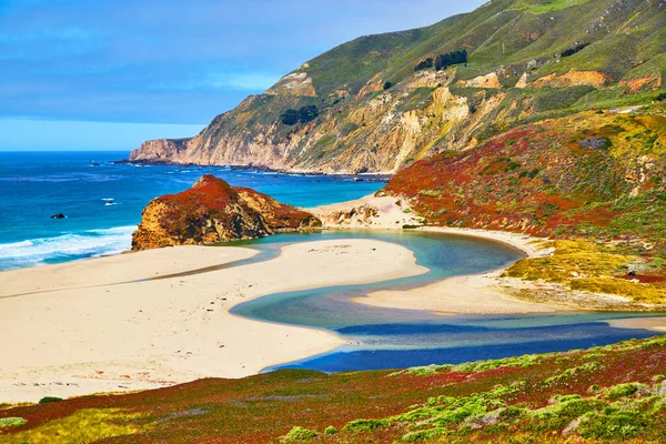 Image of Majestic blue river on ocean beach meets the ocean surrounded by hills covered in spring plants