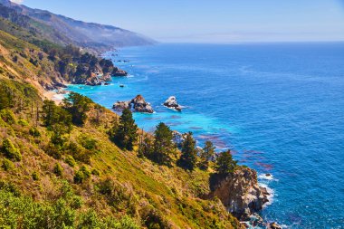 Batı kıyısında dağlar ve kayalarla dolu canlı mavi bir okyanus görüntüsü.