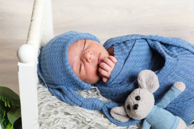 infant newborn boy swaddled in blue towel with head wrapped resting on little bed decorative flowers and leaves