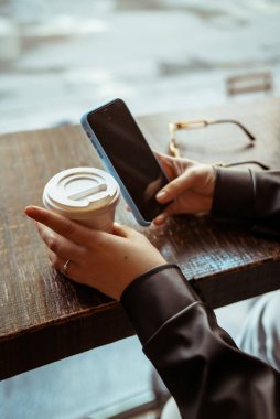 Kadın cep telefonu kullanıyor ve kafede kahve içiyor.