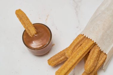 Şekerli ve tarçınlı geleneksel churro bir kase karamel ile mermer bir masada servis edilir..