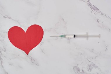 Yanında şırınga olan bir kalp. Covid-19 aşısı konsepti. Minimalist salgın senaryosu.