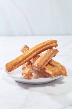 Şekerli ve tarçınlı geleneksel churro bir kase karamel ile mermer bir masada servis edilir..