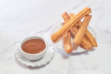 Şekerli ve tarçınlı geleneksel churro bir kase karamel ile mermer bir masada servis edilir..