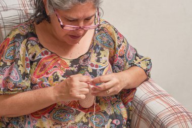 Orta yaşlı bir kadın evde rahat ve konsantre bir şekilde örgü örüyor..