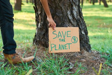 Ethnic teenage with Save The Planet inscription on cardboard piece in the forest