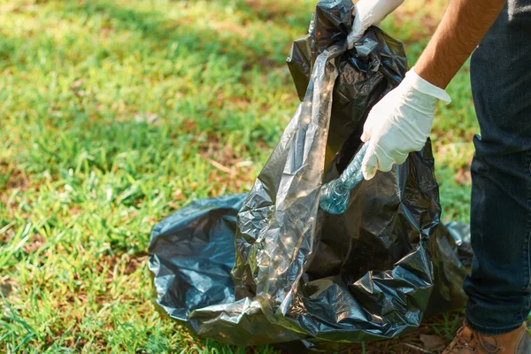 Latino teenage male volunteer picks up trash from the forest for plastic recycling.