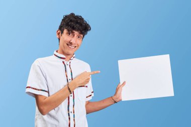 Meksika elbiseli genç Meksikalı adam beyaz ilan veriyor, mavi arka planda izole edilmiş..