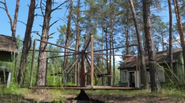 Eski paslı atlıkarınca, çam ormanındaki ahşap evlerin arka planında rüzgardan hafifçe uzaklaşır.