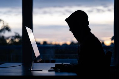 A hacker commiting digital crimes on a desktop computer. clipart