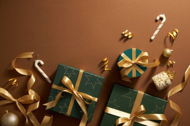 Kahverengi arkaplanda noel süsünün en üst görüntüsü, sarı kurdeleli hediye kutusu ve tatil için ortası boş parlak sarı inci.