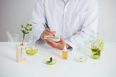 Bitkiler ve çiçekler petri kabından elde edilir ve laboratuvarda beyaz bir arka plan, test tüpünde yeşil bir yaprak ve kozmetik reklamcılığı için bilim adamı, fotoğraf bilimi konsepti