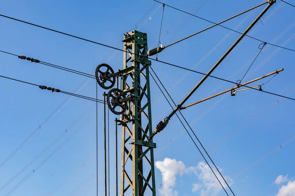 Cables, brackets and gears on a metal pole for overhead lines for electric trains against a blue sky