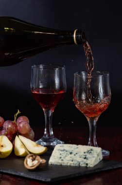 Şarap, peynir, biraz üzüm ve siyah arka planda ahşap tabakta armut.