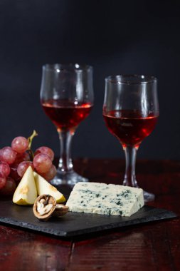 Şarap, peynir, biraz üzüm ve siyah arka planda ahşap tabakta armut.