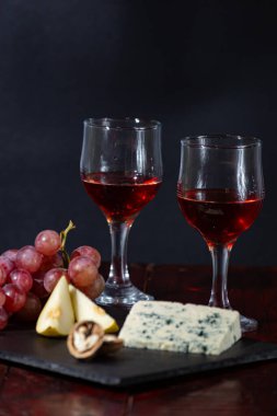 Şarap, peynir, biraz üzüm ve siyah arka planda ahşap tabakta armut.