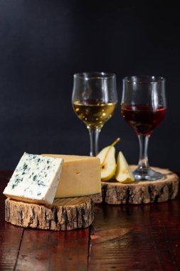 Şarap, peynir, biraz üzüm ve siyah arka planda ahşap tabakta armut.