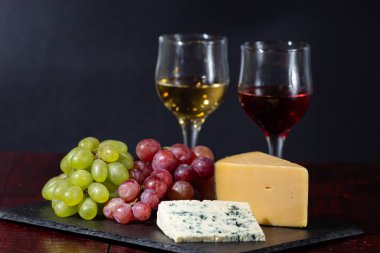 Şarap, peynir, biraz üzüm ve siyah arka planda ahşap tabakta armut.