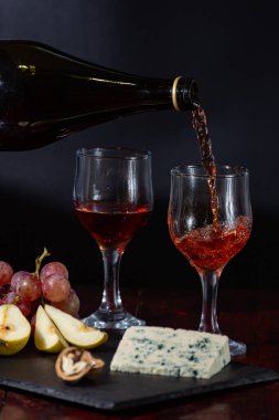 Şarap, peynir, biraz üzüm ve siyah arka planda ahşap tabakta armut.