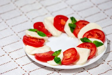 Caprese - mozzarella, domates, yeşil fesleğen beyaz bir tabakta soslu