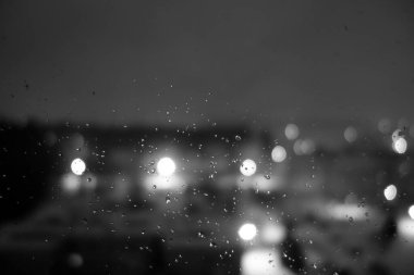 Gece şehrinde yağmur damlalarının olduğu pencereden bak. Bulanık arkaplan               
