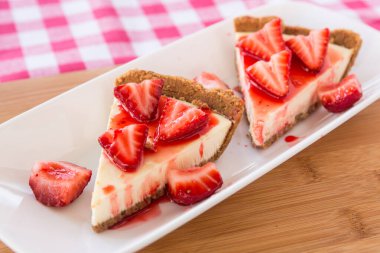 İki dilim dilimlenmiş peynirli kek ve beyaz tabakta taze çilek.