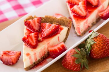 Tatlı olarak iki dilim dilimlenmiş peynirli kek ve çilek.