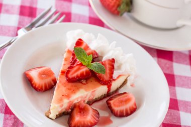Taze dilimlenmiş çilekli cheesecake, çatallı kırmızı kareli kumaş.