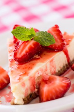 Taze peynirli kek dilimi, dilimlenmiş çilek ve nane yaprağı.