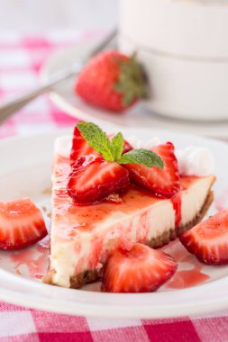 Bir dilim taze peynirli kek dilimlenmiş çilek ve bir fincan kahve.