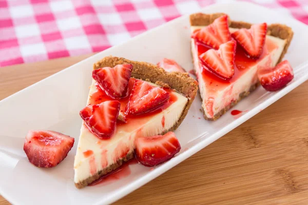 İki dilim dilimlenmiş peynirli kek ve beyaz tabakta taze çilek.
