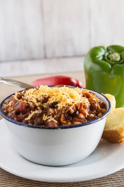 Delicious bowl of warm chili winter comfort food dinner with corn bread muffin red and green peppers vertical