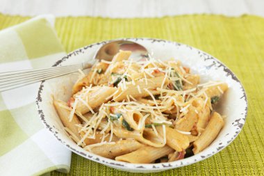 Gluten free penne pasta in a rustic bowl with parmesan cheese on top with green napkin and placemat