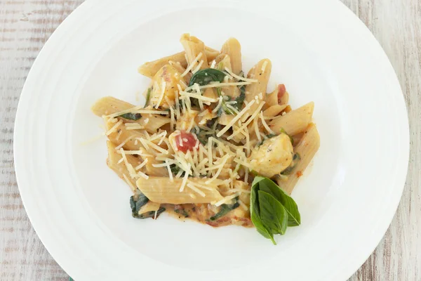 Penne pasta gluten free dinner meal with chicken, cheese, tomato cream sauce, basil on white plate from above