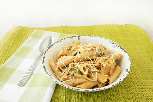 Gluten free penne pasta dinner recipe in white bowl with parmesan cheese on top with green napkin and placemat