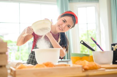 Genç ve güzel bir Asyalı kadın mutfağında, fırınında ve kahve dükkanında yemek pişiriyor. 