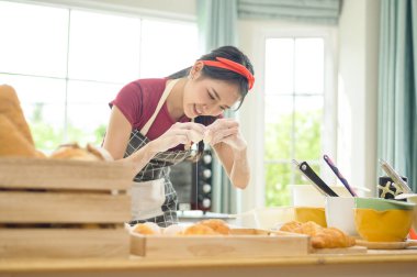 Genç ve güzel bir Asyalı kadın mutfağında, fırınında ve kahve dükkanında yemek pişiriyor. 