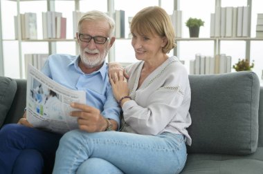 Mutlu çift Kafkasyalı son sınıf öğrencisi dinleniyor, oturma odasında gazete okuyor. 