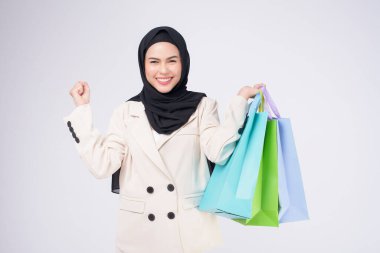 Takım elbiseli güzel Müslüman kadın beyaz arka plan stüdyosunun üzerinde renkli alışveriş çantaları tutuyor.