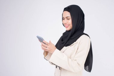 Beyaz arka planda akıllı telefon kullanan takım elbiseli güzel Müslüman kadının portresi.