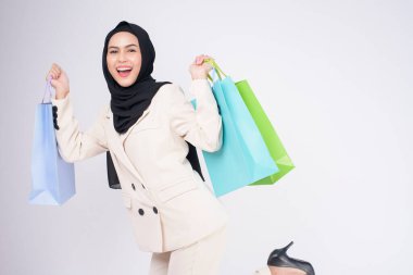 Takım elbiseli güzel Müslüman kadın beyaz arka plan stüdyosunun üzerinde renkli alışveriş çantaları tutuyor.