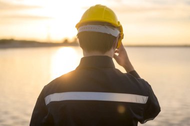 A male engineer wearing a protective helmet at sunset.	