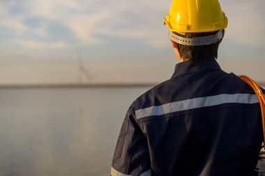 A male engineer wearing a protective helmet at sunset.	